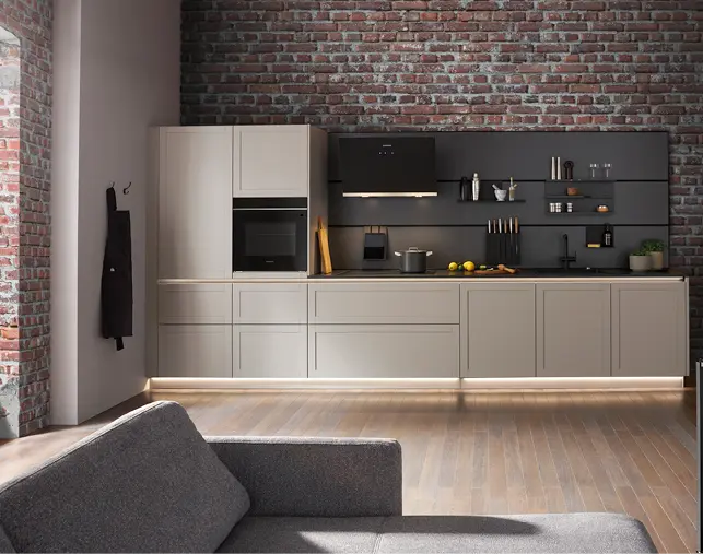 Stilvolle Einbauküche mit hellen Fronten, schwarzer Küchenrückwand und Backsteinwand im Industrial Design. Integrierter Backofen, Kochfeld und offene Regale schaffen modernes Küchendesign mit klaren Linien und viel Stauraum.